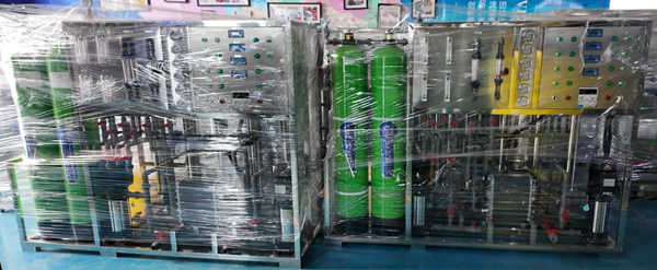 Two sets of packaged RO pure water treatment machines with green FRP filter tanks, wrapped in plastic film for shipment